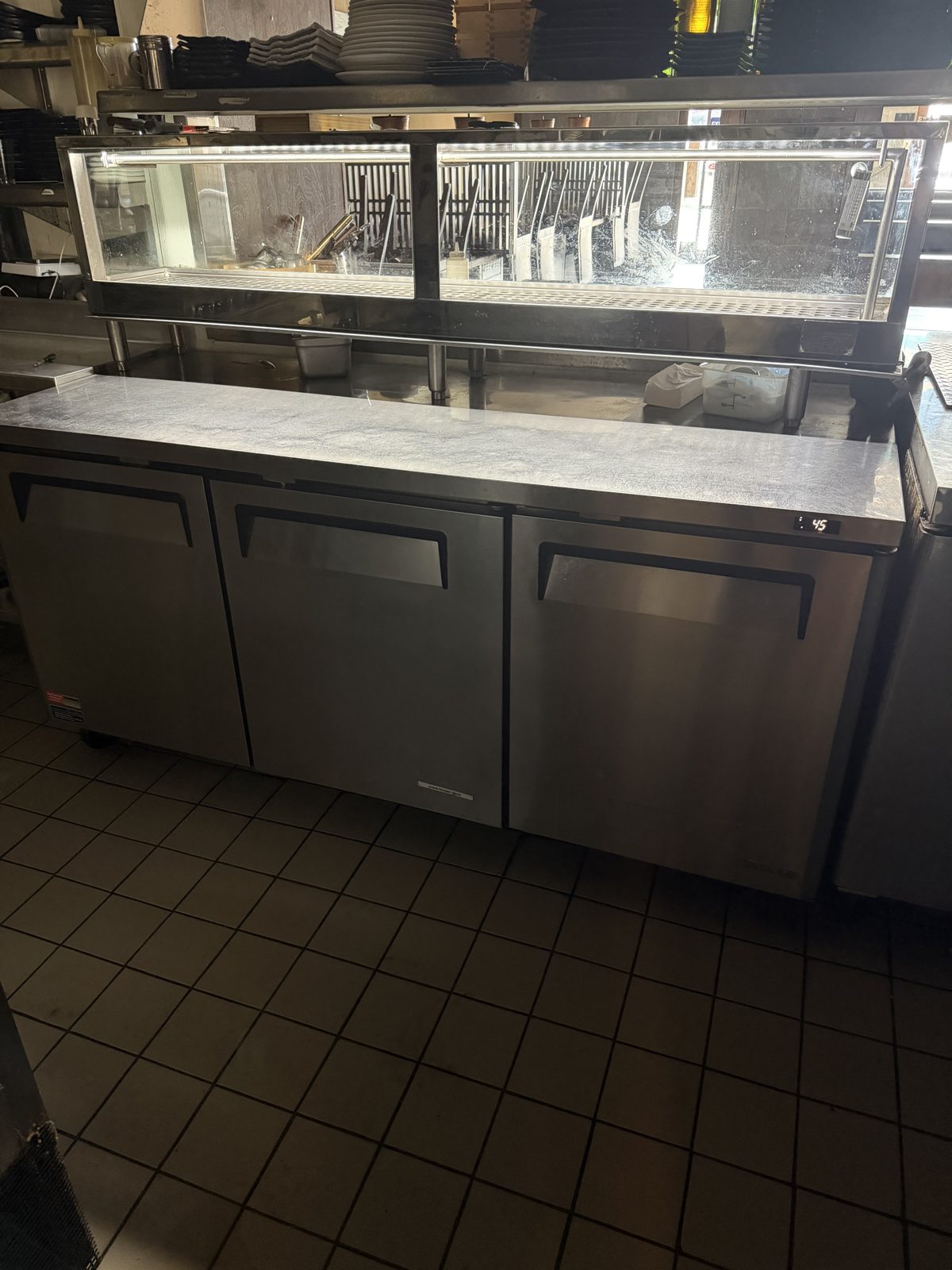 Three-door refrigerated sandwich and salad prep table holding at temperature in a commercial kitchen