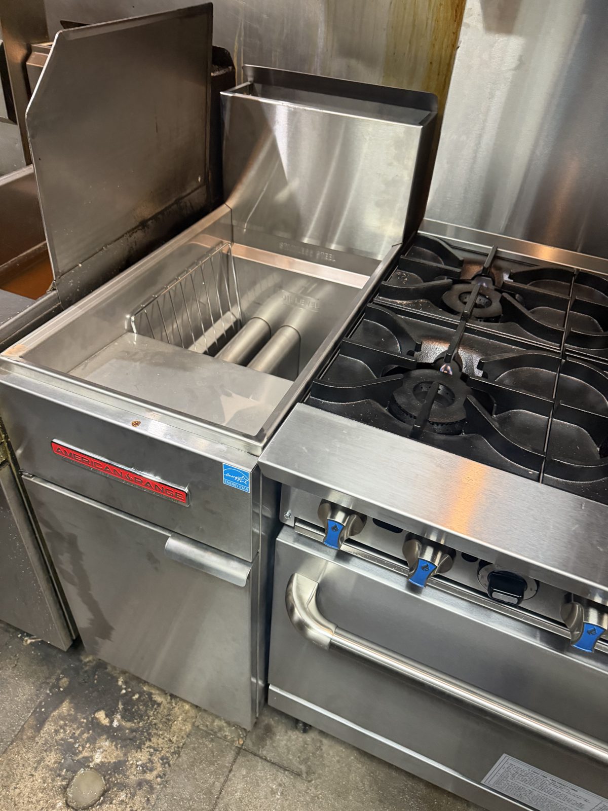 American Range commercial gas range with lit burners beside a stainless steel deep fryer